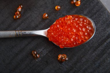 Siyah ahşap arka planda kırmızı havyarlı kaşık..