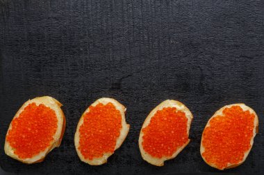 Tereyağlı, kırmızı havyar ve siyah tahtada havyarlı bir kaşık. Boşluğu kopyala.