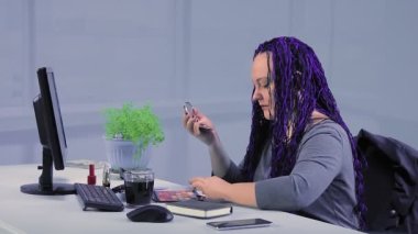 Ofiste mavi afro örgülü bir kadın gözlerini gölgelerle boyuyor.