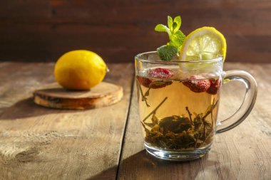 Çilekli ve ahşap masadaki limonlu cam bardakta yeşil çay. Yatay fotoğraf