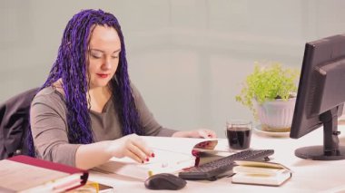 Ofiste mavi afro saç stili olan Yahudi bir kadın çok yorgun raporlarla çalışıyor. Genel plan