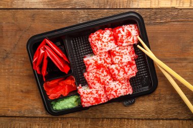 Karides, salatalık, wasabi krem peyniri ve tobiko havyarlı rulo seti ve çubukların yanındaki tahta zeminde zencefilli bir kutuya yapışıyor. Boşluğu yatay olarak kopyala