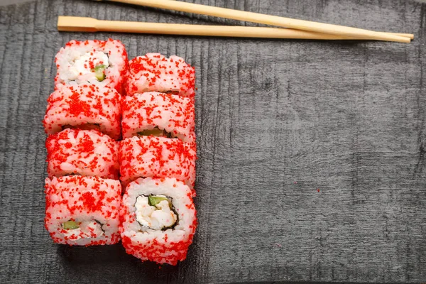 Roll with shrimp and tobiko caviar and sticks on a black board on a gray background. Copy space Horizontal photo