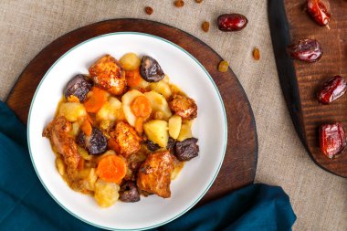Bir tabak yahudi mutfağı havuç, hurma ve hindi eti beyaz bir tabakta yuvarlak bir tahtada kurutulmuş meyvelerin yanında keten bir zemin üzerinde..