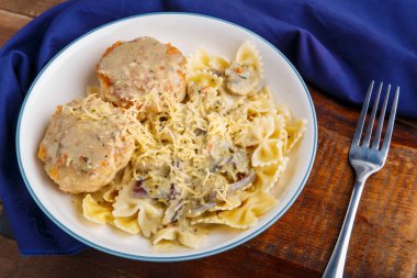 Kremalı soslu makarna, mantarlı ve bej bir tabakta tavuk köftesi ahşap bir masada, çatalın yanındaki mavi peçetede..