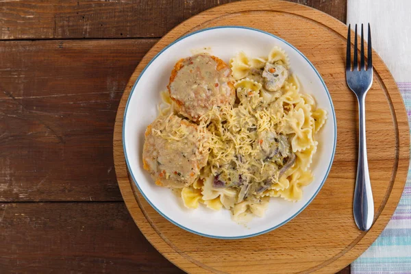 Kremalı soslu makarna, mantarlı tavuk köftesi, bej bir tabakta, ahşap bir masada, çatalla birlikte yuvarlak bir masada.