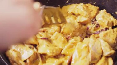 Bir kadının eli, soslu bir spatula tavuğuyla kızartma tavasında soğan karıştırıyor.