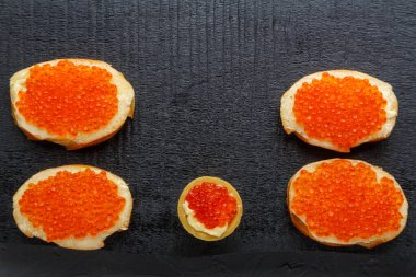 Tereyağı ve kırmızı havyarla siyah bir tahtada.