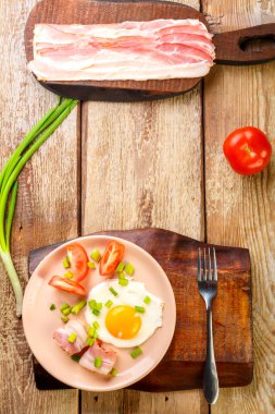 Çırpılmış yumurta, domuz pastırması, domates, soğan ve ahşap bir masada, doğranmış pastırma ve domatesin yanında..