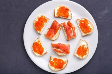 Tereyağlı, kırmızı havyarlı ve somon balıklı beyaz bir tabakta gri beton arka planda..