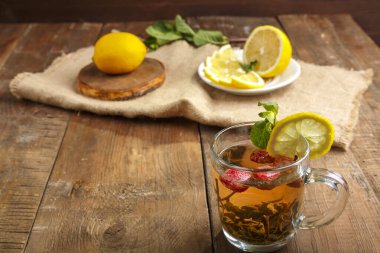 Çilekli yeşil çay, nane şekeri ve limonlu, ahşap bir masada, peçetedeki limonun yanında..