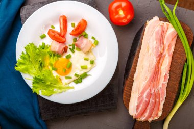 Domatesli ve yeşil soğanlı sahanda yumurta ve bir sıra doğranmış pastırma, domates ve soğanlı gri beton kaplama..