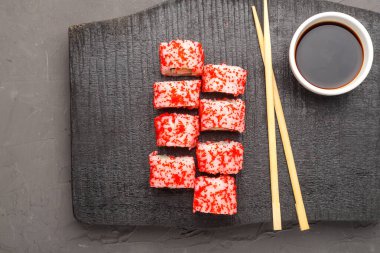 Karides salatalığı ve tobiko havyarla yuvarlan ve siyah oyulmuş bir tahta ve soya sosuyla birlikte gri bir arka planda bir sos kasesinde yuvarlan..