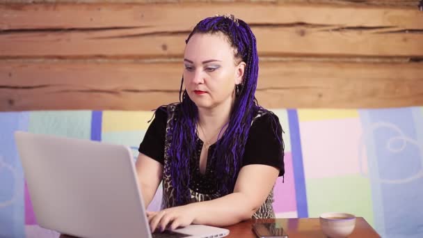 소파에 랩탑 프린트를 한 채로 책상에 앉아 있는 파란색의 아포 코스를 입은 젊은 여자 — 비디오