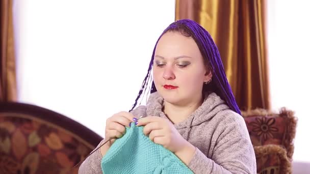 Vrouw met blauw afro kapsel breien op de bank in de kamer — Stockvideo