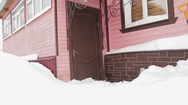 A woman in a winter coat with difficulty opens the door covered with snow and leaves the house — Stock Video