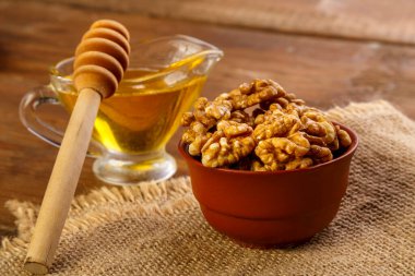 Çuval bezi üzerinde kil kasede ceviz, tahta masada kaşıkla balın yanında..