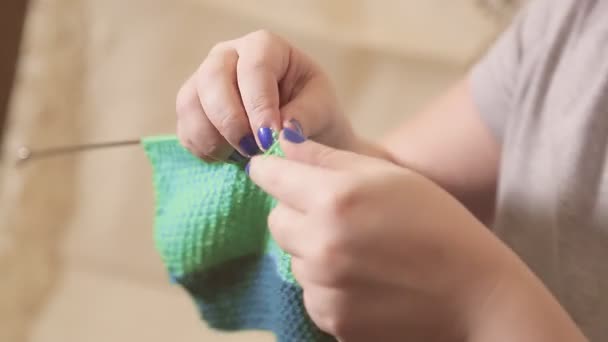 Las manos de las mujeres sostienen agujas de punto y tejen un suéter hecho de lana ligera — Vídeos de Stock