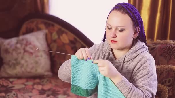 Una mujer judía con un peinado afro azul teje en el sofá — Vídeos de Stock