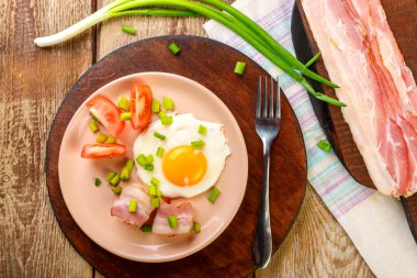 Çırpılmış yumurta, domuz pastırması, domates ve soğanlı ve ahşap bir masada, çatal, dilimlenmiş pastırma ve domatesin yanında..