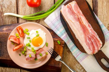 Domatesli ve yeşil soğanlı kızarmış yumurta ve doğranmış pastırma ve domateslerin yanında bir tabakta ahşap bir masa..