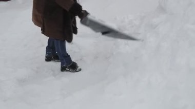 Kürekli, kalın ceketli bir kadın kar yağdıktan sonra karları temizler.