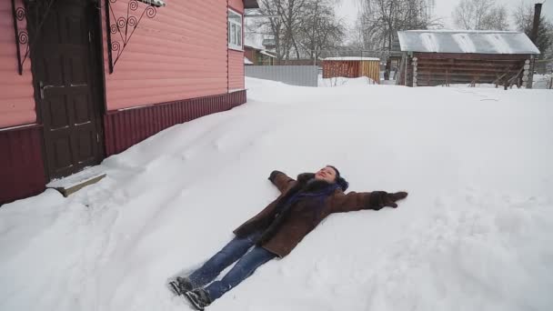 雪の中にアフロ編組の暖かいコートを着た女性が雪の中に横たわっており、冬を楽しむ — ストック動画