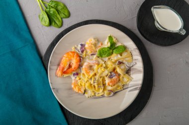 Kremalı soslu Farfalle makarnası, gri bir tabakta, beton arka planda, mavi bir peçete ve bir sürahi kremanın yanında..