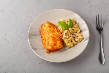 Fırında tavuk göğsü ve salata tabağında gri bir arka planda çatalın yanında..