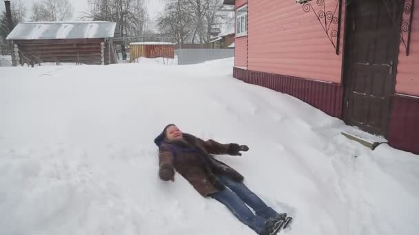 A woman in a warm coat with afro braids lies in the snow in the snow and enjoys the winter — Stock Video