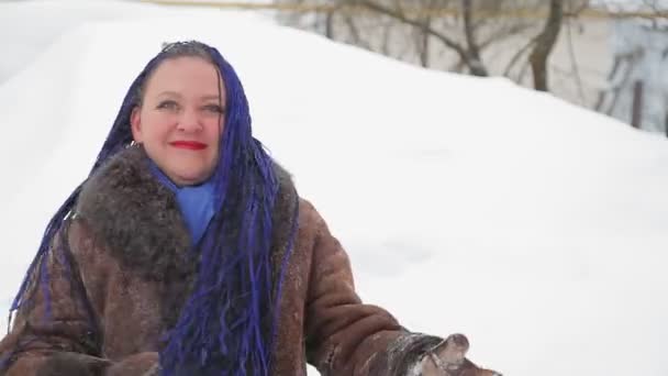 Een gelukkige vrouw in een warme jas met afro vlechten gooit sneeuw voor haar neus — Stockvideo