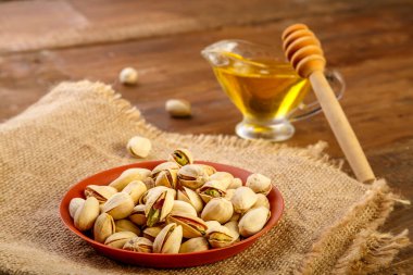 Kahverengi bir klozetin içindeki şam fıstığı. Tahta bir masada kaşıkla balın yanında..