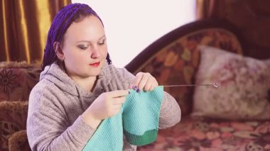 Kanepeye örgü ören mavi afro saçlı Yahudi bir kadın.