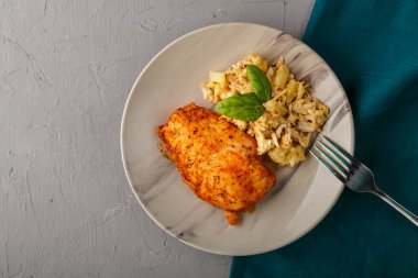 Fırında tavuk göğsü, salata ve tabakta ıspanakla süslenmiş mavi peçete standındaki gri arka planda bir çatalın yanında..