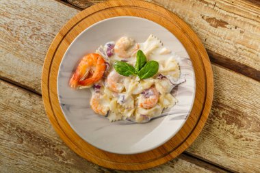 Kremalı soslu karidesli Farfalle makarnası. Yuvarlak stanttaki ahşap bir masada gri bir tabakta. Yatay fotoğraf