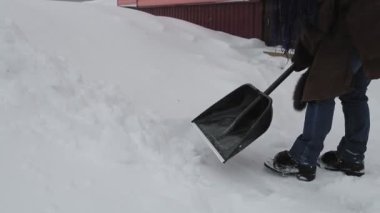 Elinde kürekle kalın bir palto olan bir kadın evinin bahçesinde kar yağdıktan sonra karları temizler. Genel plan