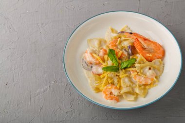 Beton arka planda gri bir tabakta kremalı soslu karidesli makarna. Uzayı yatay olarak kopyala