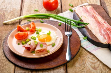 Çırpılmış yumurta, domuz pastırması, domates ve yeşil soğan ve ahşap bir tabakta, çatalla, doğranmış pastırma ve domateslerin yanında. Yatay fotoğraf