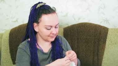 Kanepedeki mavi saçlı gelin, gelinliğini bir iğne ve iplikle elleriyle dikiyor..