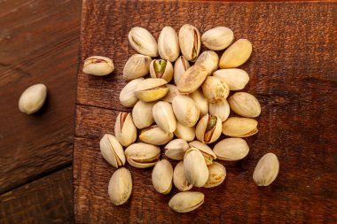 Ahşap bir masanın üzerindeki kare tahtaya saçılmış fıstıklar..