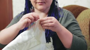 Kanepede oturan gelin, kendisi için bir iğne ve iplikle bir gelinlik dikiyor..