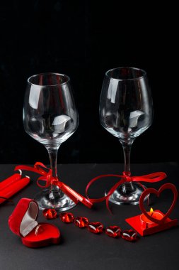Siyah arka planda kurdeleli iki şampanya kadehi, kalp şeklinde bir kutunun yanında yüzük ve mumlu bir şamdan..