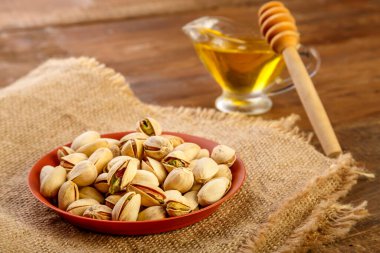 Kahverengi bir klozetin içindeki şam fıstığı. Tahta bir masada kaşıkla balın yanında..