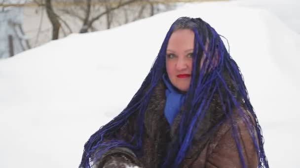 Een vrouw in een warme jas met afro vlechten gooit sneeuw voor haar neus — Stockvideo