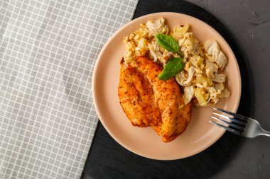 Fırında tavuk göğsü, salata ve tabakta ıspanakla süslenmiş gri peçetedeki beton arka plandaki çatalın yanında..