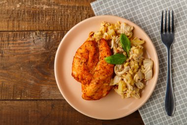 Bej bir tabakta fırında tavuk göğsü ve peçetedeki ananas salatası bir çatalın yanında.