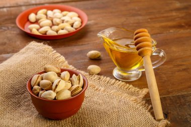 Çuval bezi üzerinde fıstıklar, tahta bir masada kaşıkla balın yanında..