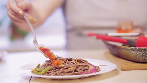 Une main de femme verse la sauce d'une cuillère de soba avec des champignons et des légumes dans une assiette — Video