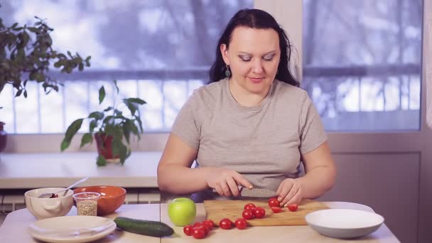 Egy barna nő a konyhaasztalnál cseresznyés paradicsomot vág salátának. — Stock videók