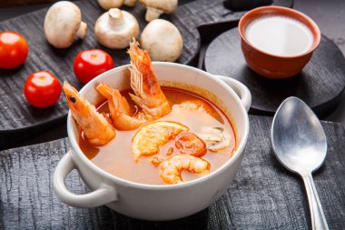 Ahşap tezgahta hindistan cevizi sütü domatesli ve mantarlı bir kasenin yanında beton bir arka planda karidesli Tom tatlı patates çorbası..